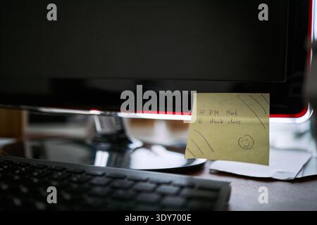 Closeup showing computer monitor with yellow sticky note attached displaying handwritten reminders for meeting and work class, keyboard visible in foreground, office cleaning context implied Stock Photo