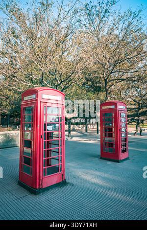 Red telephone boxes stand in a park on a clear day in Buenos Aires, Argentina with trees in the background Stock Photo