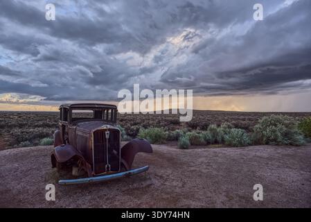 Old Model-T marks Route 66 with storm clouds forming over the Arizona landscape in Petrified Forest National Park Stock Photo