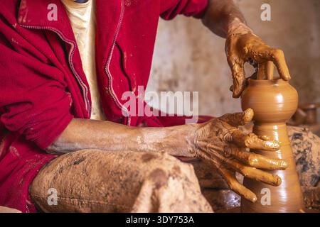 Potter shapes clay in workshop while working diligently in Safi, Morocco with mud-covered hands and focused expression Stock Photo