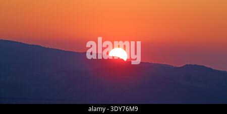 View of sunrise over distant hills in Utah showing bright sun rising in the morning light Stock Photo