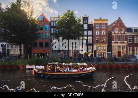 Canals in Amsterdam with a boat during sunset in North Holland showing houses and trees along the water Stock Photo