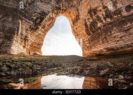 View from inside a sea cave in Normandy showing a chalk arch and weathered rocks at Etretat during daylight hours Stock Photo