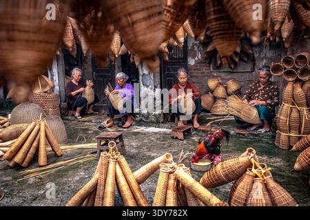 Women craft bamboo fish traps in Hanoi, Vietnam, showcasing skills inherited through generations in a traditional workshop setting Stock Photo