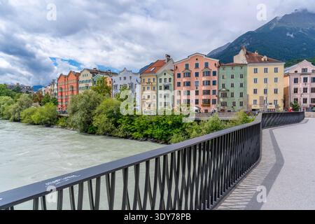 Bright buildings line the River Inn under sunny skies in summer in Tyrol Region of Austria Stock Photo