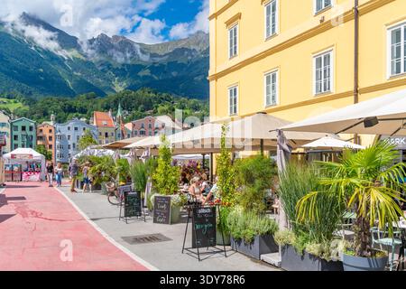 Visitors enjoy lunch at a restaurant along colorful buildings by River Inn in summer in Tyrol Region of Austria Stock Photo