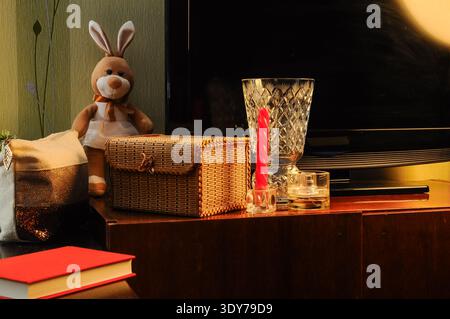 A still life arrangement featuring a stuffed bunny, a decorative woven box, a crystal vase, a red candle in a holder, and a bottle of perfume on a woo Stock Photo