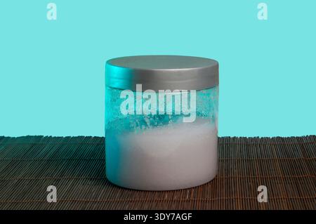 A clear plastic container holds a white, textured substance, illuminated by cool blue and green lighting, set against a solid cyan backdrop on a woven Stock Photo