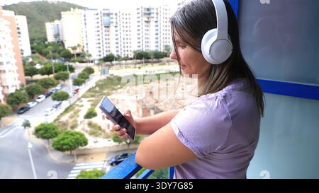 Woman with long hair wearing headphones listens to music on smartphone  Stock Photo