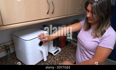 Woman using air fryer in modern kitchen, countertop with various kitchen appliances  Stock Photo