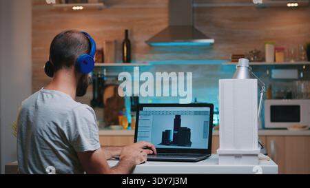 Man designer using cad software to design a 3D concept of buildings working overtime from home. Industrial male employee studying prototype idea on personal computer looking on device display Stock Photo