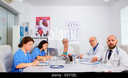 Team of doctors discussing online with chief phisycian, training medical workers group, teaching medic team in virtual conference web camera. Medic having video conference sitting in hospital office Stock Photo