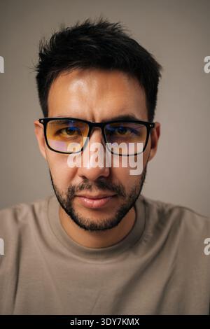 Close-up vertical portrait of young man wearing anti-fatigue glasses with focused and concerned expression, showcasing deep thought and concentration Stock Photo