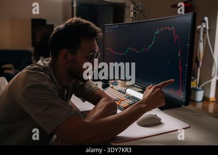 Young man monitoring stock market financial charts displaying significant price drop on computer screen, representing crisis, loss, challenging Stock Photo