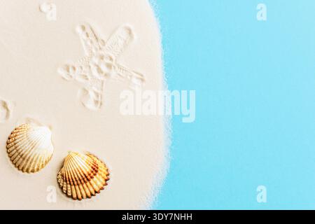 Seashells on sand near blue sea with starfish imprint. Summer vacation concept. Top view, flat lay, copy space Stock Photo
