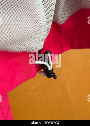 Drawstring detail on red jacket close-up with beige textured background. Mobile photo Stock Photo