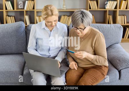 Senior woman paying online with help, credit card and laptop on sofa at home Stock Photo