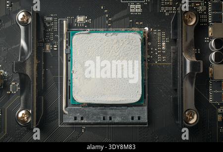 used computer motherboard and installed cpu covered in grey thermal paste, textured compound surface in full frame in top view, pc maintenance concept Stock Photo