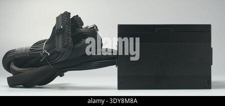 black computer power supply unit isolated neutral gray background, bundled braided cables and connectors for psu, mock-up template side view Stock Photo