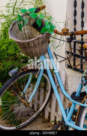 Antique bicycle with a wicker basket on the front in front of a rustic house. Stock Photo