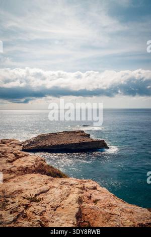 Sunlit Rocky Coastline Over Calm Blue Ocean With Dramatic Cloud Horizon And Serene Seascape View Stock Photo