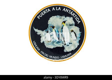 Round sticker showing emperor penguins standing on antarctic ice with map silhouette; spanish text reads 'puerta a la antartida' and 'ushuaia - fin de Stock Photo