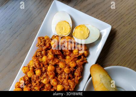 Plate of spiced chickpea and minced meat stew with two halved boiled eggs and bread on wooden table Stock Photo