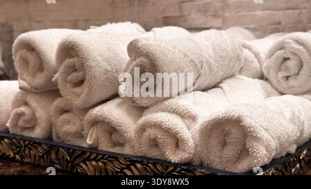 A stack of soft, white towels rolled up and neatly arranged in a luxurious setting, perfect for high-end hotels, spas, or elegant bathrooms. Stock Photo