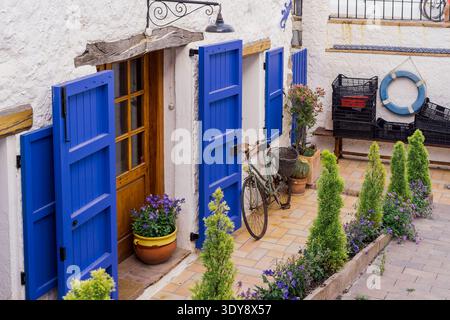 Charming mediterranean courtyard with white stucco walls, bright blue wooden shutters and doors, potted flowering plants, bicycle leaning against wall Stock Photo