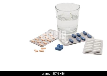 Various blister packs with beige, blue, and white pills scattered near a glass of water on white background Stock Photo