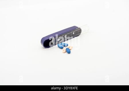 Small pill organizer and scattered blue and pink tablets on white background, minimal medical still life, high-key lighting Stock Photo