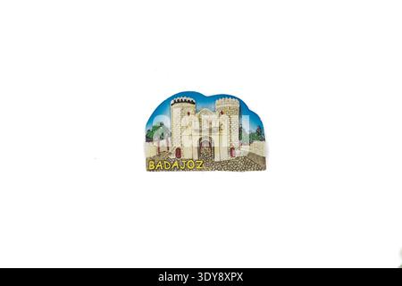 Decorative magnet showing a stone fortress gate with two round towers under blue sky, with trees and cobbled path, labeled 'badajoz'. Stock Photo