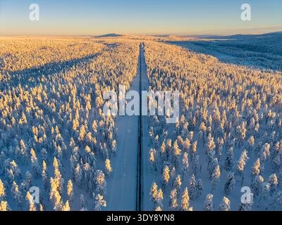 Snow blankets the serene landscape of Akaslompolo in Lapland, Finland, where a long, winding road stretches through a forest of frosty trees, creating a tranquil winter escape. Stock Photo