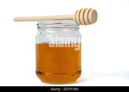 Glass jar of honey with wooden dipper on top. Organic sweetener, minimal food photography on white background.  Stock Photo