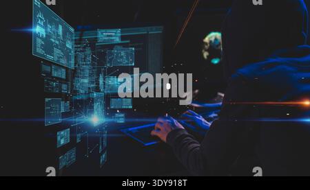 A hooded figure works intently on a luminous keyboard in a dark digital environment, surrounded by a complex holographic interface showcasing Stock Photo