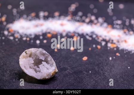 Geode crystal showing inner formations with white and pink Himalayan salt spread on a dark surface Stock Photo