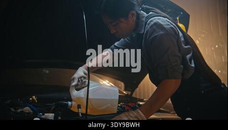 Professional Woman Auto Technician Refills Automotive Fluid Under Hood in Modern Workshop. Wearing Protective Gloves, Young Female Performs Routine Car Service With Confidence and Technical Expertise. Stock Photo