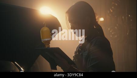 Asian Female Professional Performs Final System Sweep Using Wireless Diagnostic Tablet. Woman Seen Clearing Dashboard Warning Lights and Updating Digital Service Log With Technical Specifications. Stock Photo