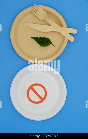 Disposable wooden and plastic plate with forbidden sign on blue background. Eco-friendly materials. No single-use plastics. Save the planet Stock Photo