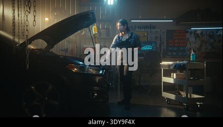 Woman Technician Performs Digital Vehicle Diagnostics, Laptop Open On Engine Bay While Tablet Assists With AI Based Troubleshooting. Female Reviews Parameters, Searches For Optimal Repair Solutions. Stock Photo