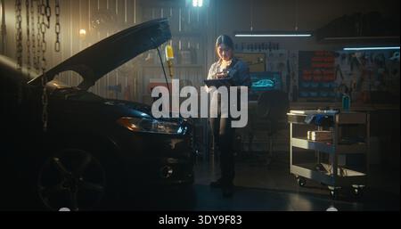 Woman Technician Performs Digital Vehicle Diagnostics, Laptop Open On Engine Bay While Tablet Assists With AI Based Troubleshooting. Female Reviews Parameters, Searches For Optimal Repair Solutions. Stock Photo