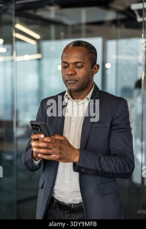 Focused man in a business suit holding and typing on his mobile phone in a contemporary workspace, managing communications and staying connected for work tasks Stock Photo