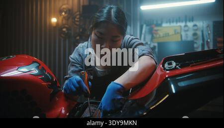 Focused Female Repairs Sport Bike Inside Garage, Carefully Using Screwdriver Place Electronic Wires Back Into Housing and Concentrating on Precise Electrical Assembly. Concept of Technical Expertise. Stock Photo