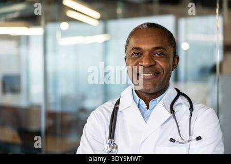 Mature african american male doctor in lab coat with stethoscope, smiling confidently for a professional portrait that conveys expertise, trust and compassionate patient care in clinic Stock Photo