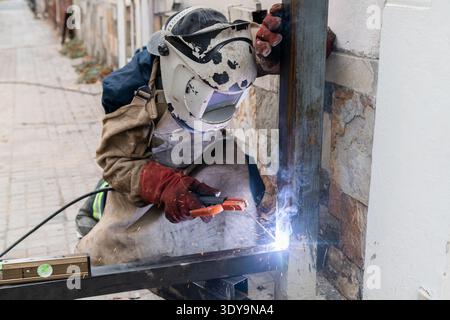 Welder wearing protective gear working on a metal column, creating sparks Stock Photo
