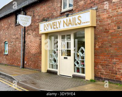 Exterior of the ‘Lovely Nails’ nail salon in Stratford-upon-Avon, UK, showing yellow shopfront, brick building, and entrance. Stock Photo