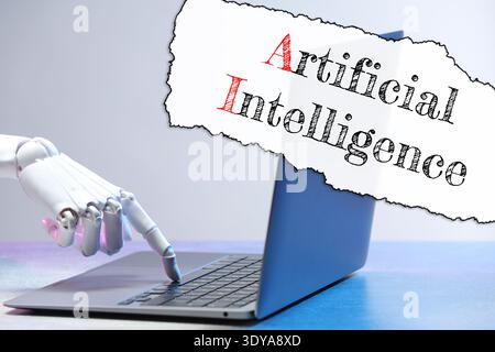 Robot using laptop. Text Artificial Intelligence on torn paper Stock Photo
