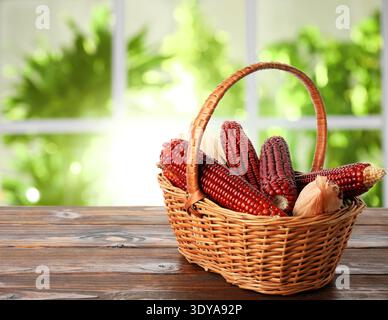 Red corn cobs in basket on wooden table indoors, space for text Stock Photo