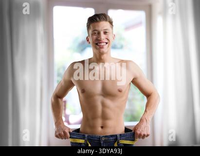 Happy man in his old jeans showing weight loss result at home Stock Photo