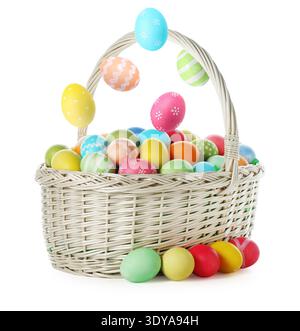 Bright Easter eggs falling into basket on white background Stock Photo